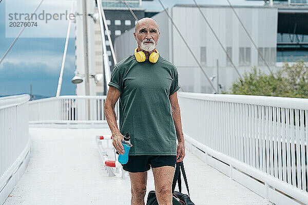 Rentner älterer Mann läuft mit Energy-Drink-Flasche und Beutel auf der Fußgängerbrücke