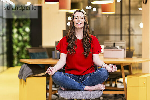 Reife Geschäftsfrau meditiert auf einem Stuhl im Büro