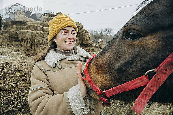 Happy woman standing with bay horse in farm