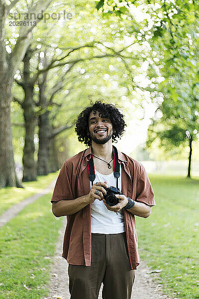 Lächelnder Mann hält Kamera in der Hand und steht im Park