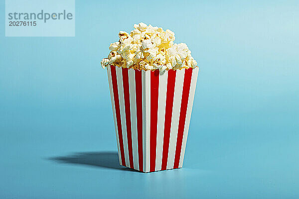 Popcorn in gestreiftem Behälter auf blauem Hintergrund