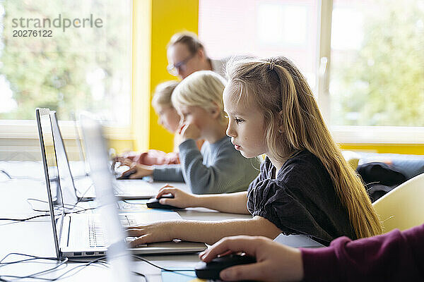 Blond girl using laptop learning computer programming in classroom