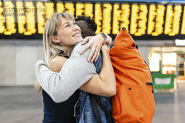 Lächelnde junge Frau umarmt Freund am Bahnhof