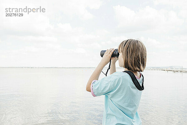 Mädchen schaut durch ein Fernglas auf den See