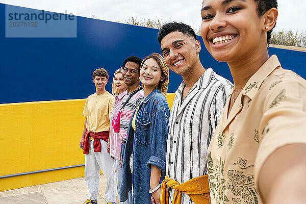 Eine multiethnische Gruppe junger Freunde steht lächelnd vor einer bunten Wand