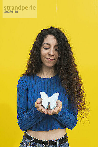 Frau hält Schmetterling in den Händen vor gelbem Hintergrund