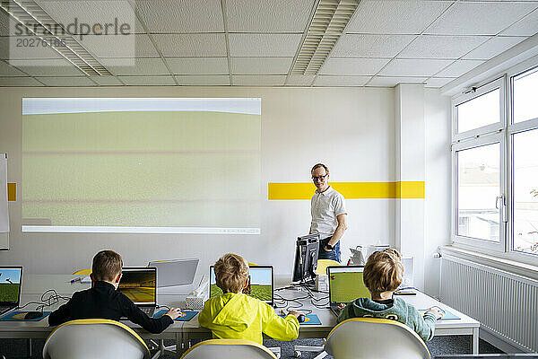 Professor teaching boys in computer classroom at school