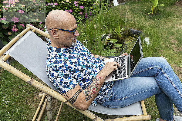 Reifer Freiberufler tippt im Garten am Laptop