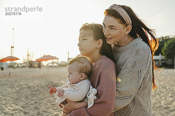 Mutter umarmt Töchter am Strand