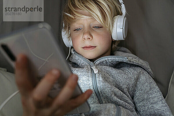 Junge trägt Kopfhörer und nutzt zu Hause das Internet auf dem Smartphone