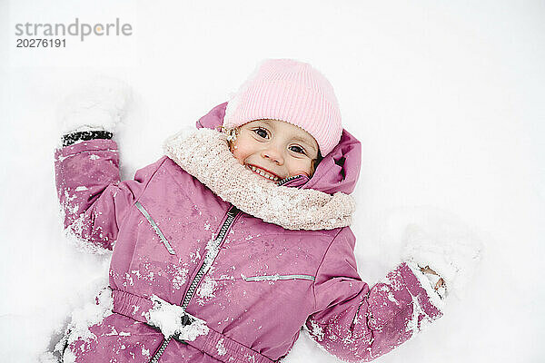 Verspieltes Mädchen trägt Winterjacke und liegt auf Schnee