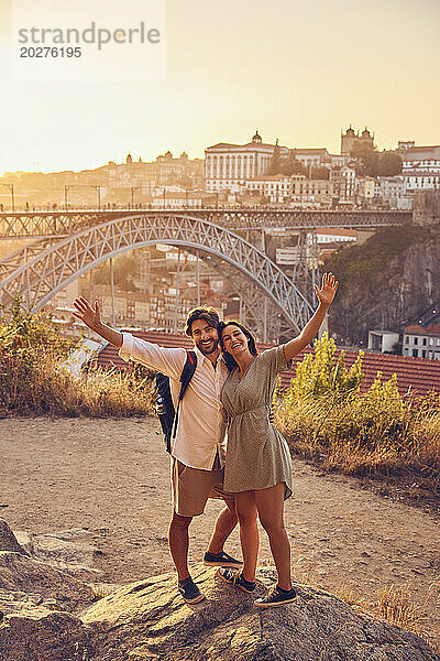 Fröhliches Paar mit erhobenen Armen vor der Dom-Luis-Brücke bei Sonnenuntergang  Porto  Portugal