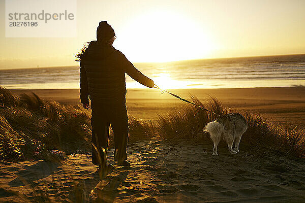 Young woman walking dog at beach