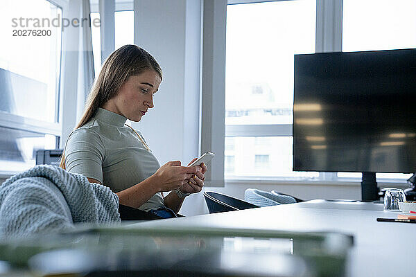 Geschäftsfrau sitzt und benutzt Smartphone im Büro