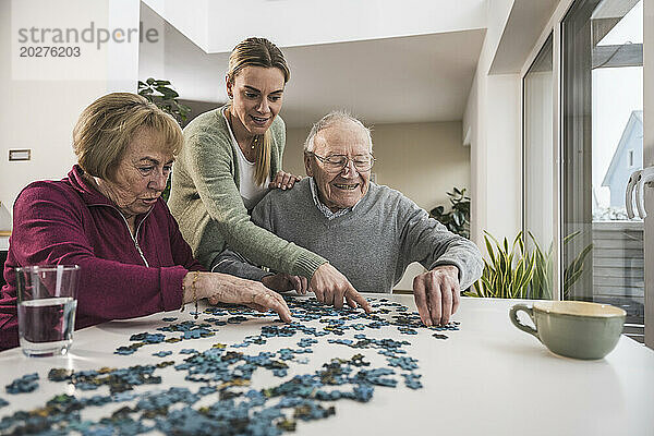 Glückliche Heimpflegerin  die mit einem älteren Paar ein Puzzlespiel spielt