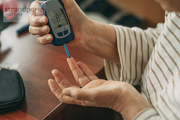 Ältere Frau misst zu Hause den Blutzuckerspiegel mit einem Glukometer