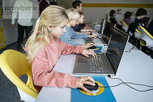 Engagiertes blondes Mädchen benutzt Laptop-Lerncomputer am Schreibtisch im Klassenzimmer