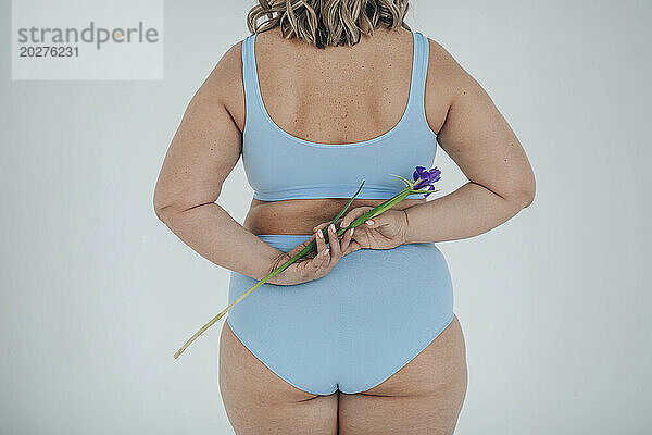 Üppige Frau versteckt blaue Irisblume vor weißem Hintergrund