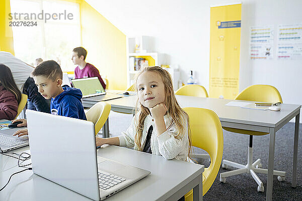 Mädchen sitzt mit der Hand am Kinn und benutzt Laptop im Computerklassenzimmer der Schule