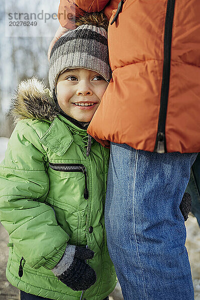 Lächelnder Junge mit Strickmütze steht im Winter mit seinem Vater