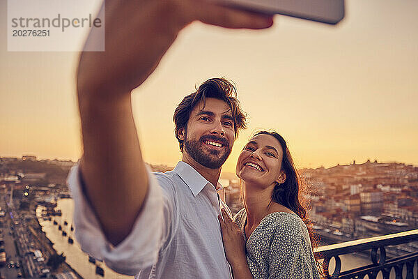Happy couple taking selfie through smart phone in front of Porto city at sunset  Portugal