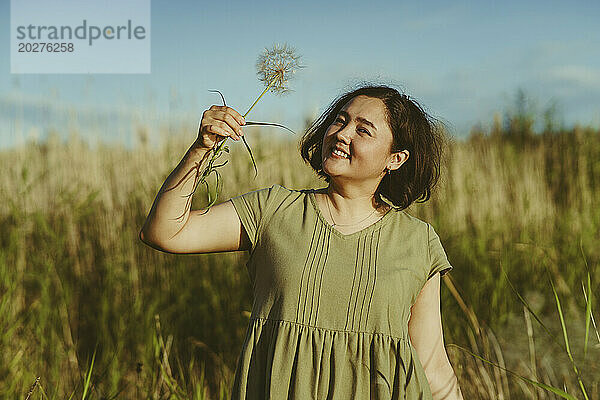 Lächelnde reife Frau hält an einem sonnigen Tag Löwenzahn im Feld