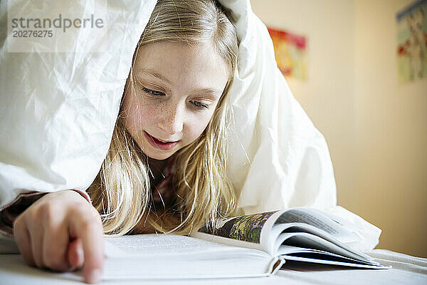 Blond covered covered in blanket reading book at home