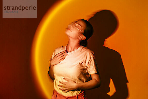 Junge Frau in Neonbeleuchtung vor orangefarbenem Hintergrund