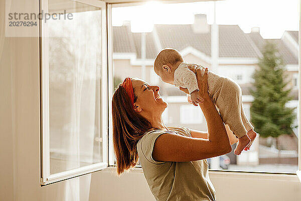 Glückliche Frau  die mit ihrer kleinen Tochter am Fenster spielt