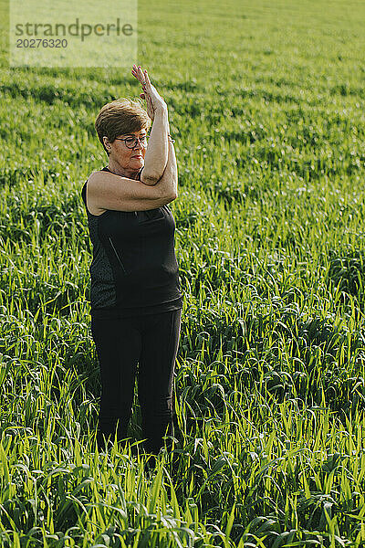 Fit retired senior woman practicing yoga in meadow