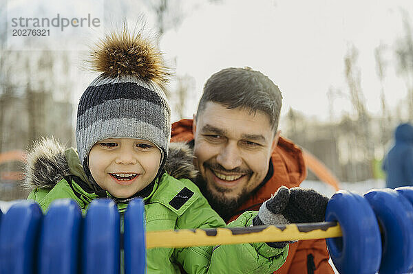 Lächelnder Mann  der im Winter mit seinem Sohn im Park spielt