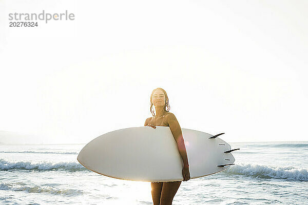 Junge Frau trägt Surfbrett am Strand