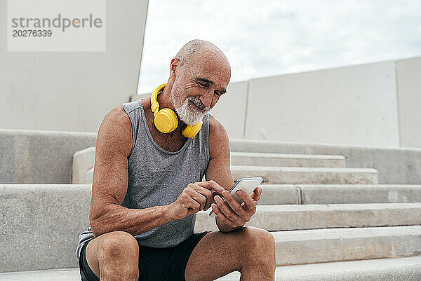 Lächelnder älterer Mann sitzt auf der Treppe und nutzt sein Smartphone