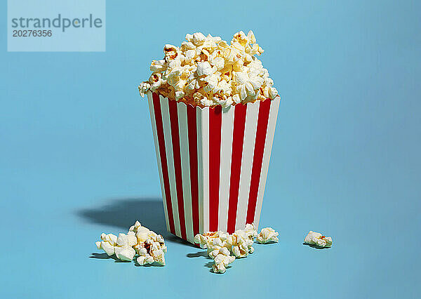 Popcorn in rot gestreiftem Behälter vor blauem Hintergrund