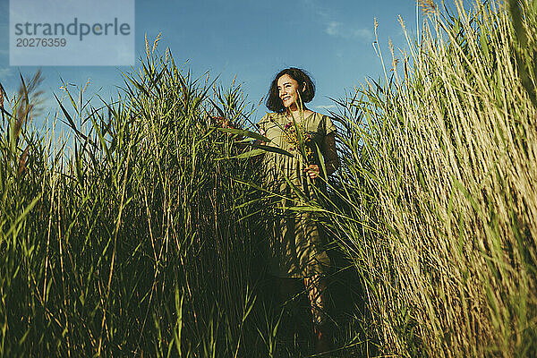 Sorglose reife Frau steht inmitten von hohem Gras auf dem Feld