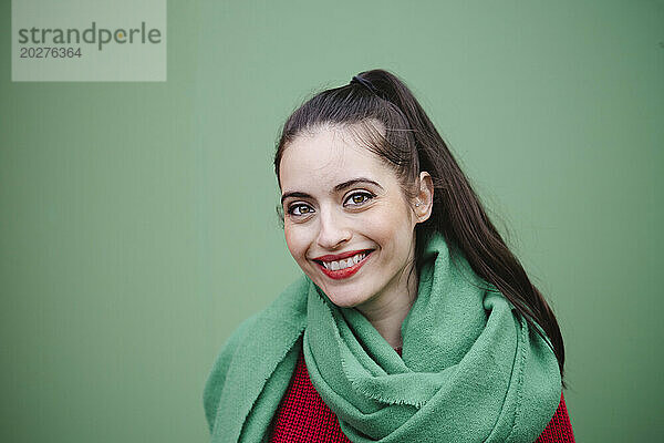 Glückliche schöne Frau mit Schal vor grünem Hintergrund
