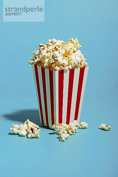 Popcorn in rot gestreiftem Behälter auf blauem Hintergrund