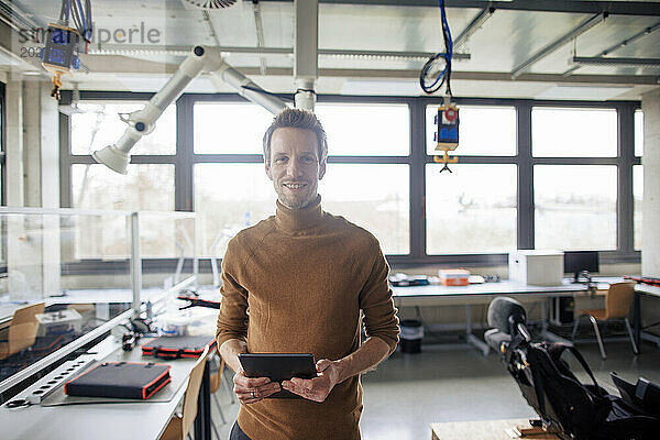 Lächelnder Ingenieur hält Tablet in der Hand und steht in der Werkstatt