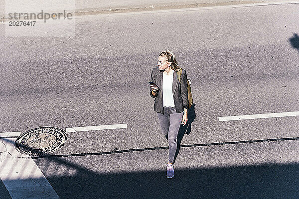 Geschäftsfrau überquert Straße an sonnigem Tag