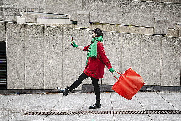 Frau läuft mit orangefarbener Tasche und macht ein Selfie mit dem Smartphone