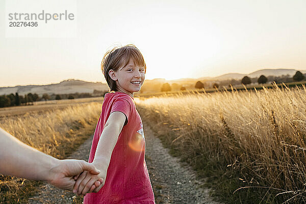 Glückliches Mädchen  das die Hand seines Vaters hält und bei Sonnenuntergang im Feld spaziert