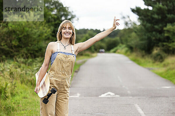 Fröhliche schöne Frau hält Skateboard in der Hand und begrüßt die Fahrt auf der Straße