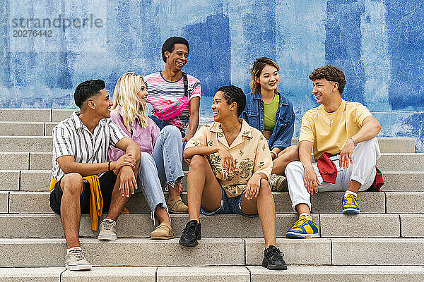 Eine multiethnische Gruppe junger Menschen sitzt auf Stufen vor einer Mauer