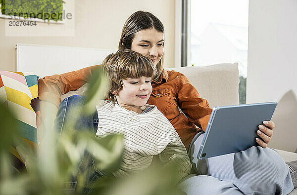 Happy mother and son using tablet PC on sofa at home