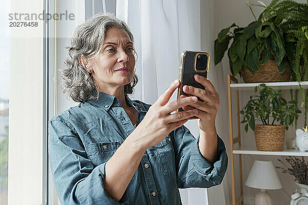 Reife Frau benutzt Smartphone zu Hause