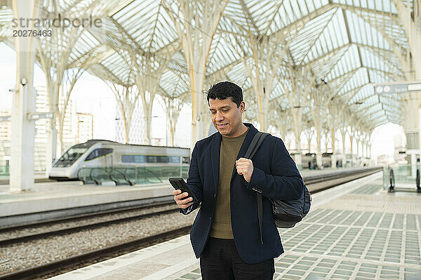 Smiling businessman using smart phone at station platform
