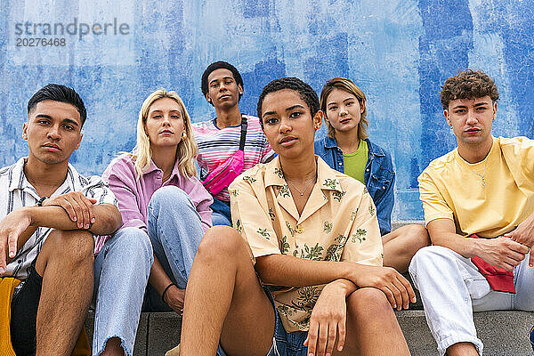 Confident young people sitting on steps in front of wall
