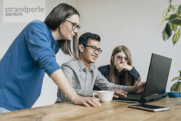 Lächelnder Programmierer diskutiert beim Start mit Kollegen am Laptop über Codierung