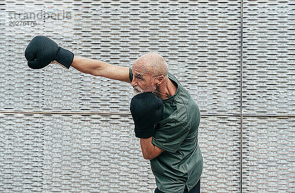 Rentner älterer Mann übt mit Boxhandschuhen am Zaun