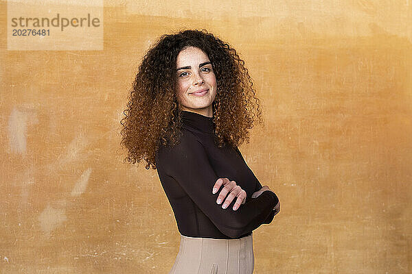 Smiling woman standing with arms crossed against brown background